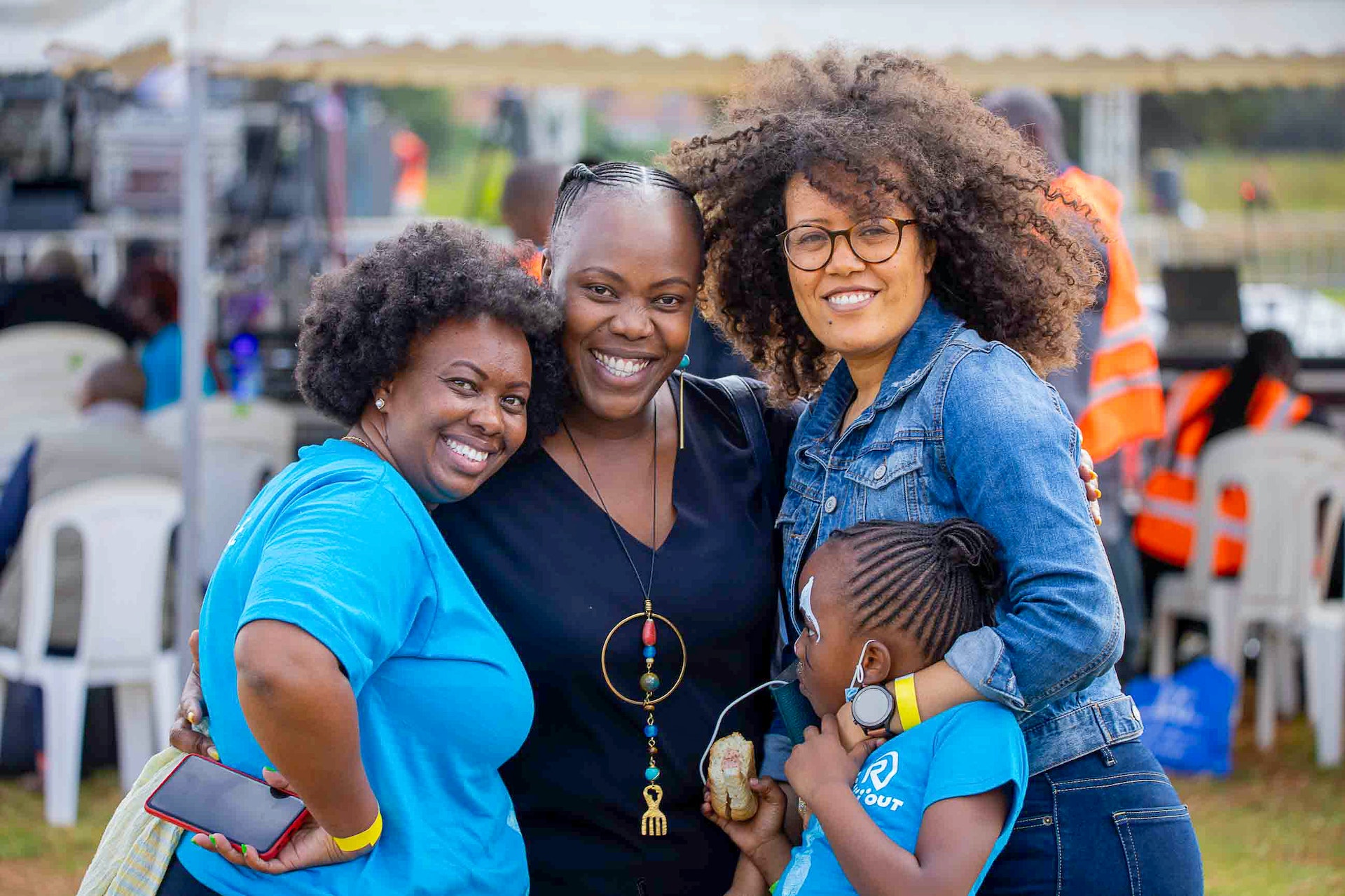 Three women and a child squeeze together smiling at an outdoor festival